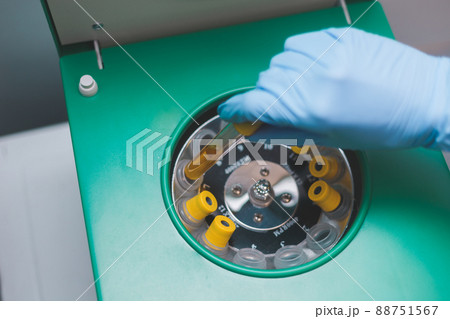 Laboratory assistant inserts tube with urine into medical centrifuge to separate it into fractions for testing. Laboratory assistant inserts tube with urine into medical centrifuge to separate it into fractions for testing. 88751567