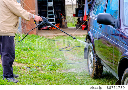 A gray-haired elderly man washes a car outdoors with a high-pressure apparatus. A gray-haired elderly man washes a car outdoors with a high-pressure apparatus. 88751789