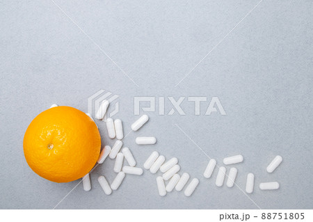 Top view on white big oval pills and ripe orange on a gray background. 88751805