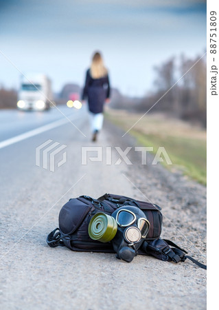 A black gas mask and a backpack lie on the side of an asphalt highway.  88751809