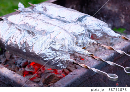 The meat on metal skewers is wrapped in aluminum foil and grilled on charcoal. 88751878