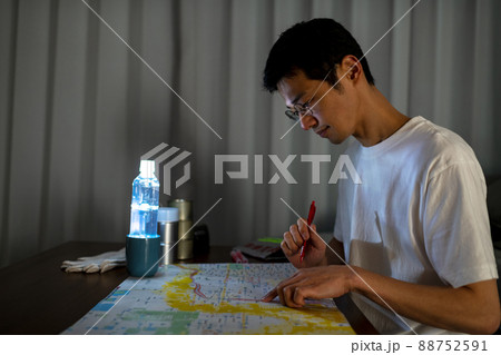 ペットボトルランタンの照明下でハザードマップを見ながら避難経路を確認している男性 88752591