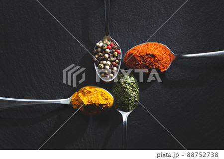 Spoons with pepper, paprika, parsley and turmeric on black background with copy space, top view. Cooking ingredients and condiments concept. Spoons with pepper, paprika, parsley and turmeric on black background with copy space, top view. Cooking ingredients and condiments concept. 88752738