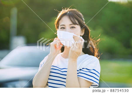 屋外でマスクを外す笑顔の若い女性 88754530