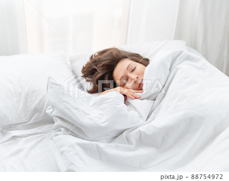 Caucasian woman is sleeping in bed. Healthy sleep on white bed linen. Morning at cozy home. 88754972