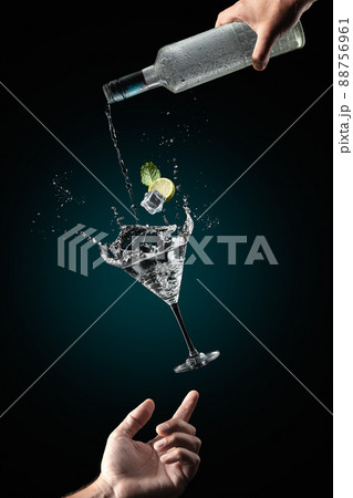 Mans hand support flying glass of cocktail drink with splash on dark blue background. Gravity concept. 88756961
