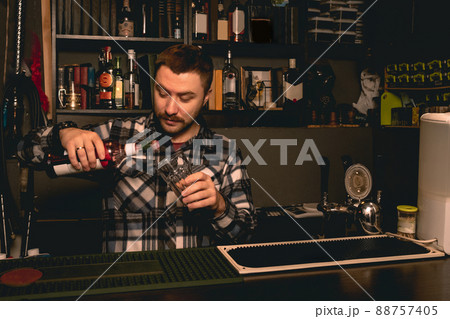 Bartender preparing cocktail behind bar counter, pouring berry liquor into glass 88757405