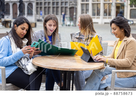 Diverse group of young business woman discussing something on a laptop in a bar courtyard after work 88758673
