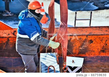 Professional slinger in construction helmet at factory unloads cargo. Boot training. Worker in warm Professional slinger in construction helmet at factory unloads cargo. Boot training. Worker in warm 88759630