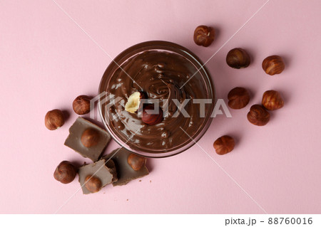 Bowl with chocolate paste, nuts and chocolate on pink background 88760016