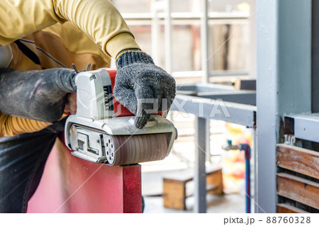 Carpenter is shaving red wood door by his shaving machine in outdoor field with steel pole building structure environment. Carpenter is shaving red wood door by his shaving machine in outdoor field with steel pole building structure environment. 88760328