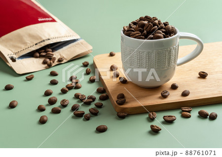Roasted coffee beans in a small white cup on a pastel green background. 88761071