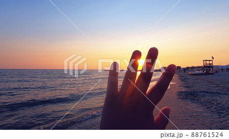 Girl looks at sun through her fingers at sunset at dawn on seashore close-up. 88761524