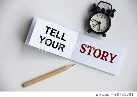 Tell your story text on notepad with alarm clock and pencil on white background. Conceptual 88761901