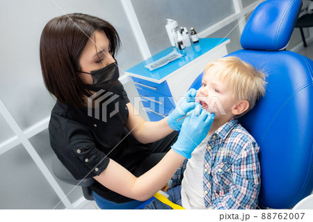 A cute little boy sits at the dentist, opened his mouth, showing his teeth to the dentist. Happy boy is sitting in the dentist's chair. Dentist - young brunette woman 88762007