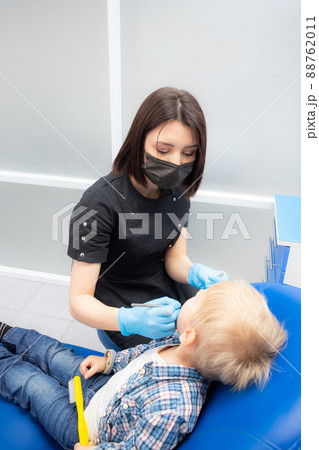 A cute little boy sits at the dentist, opened his mouth, showing his teeth to the dentist. Happy boy is sitting in the dentist's chair. Dentist - young brunette woman 88762011