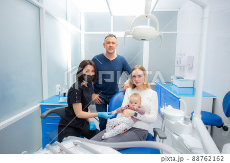 Young parents and their daughter visit a dentist to examine milk teeth. Baby at the first appointment with the dentist. Inspection of the formation of jaws, eruption of milk teeth. 88762162