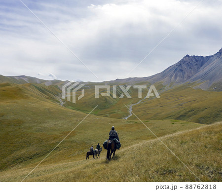 Riders with weapons on three horses move in mountainous terrain. 88762818