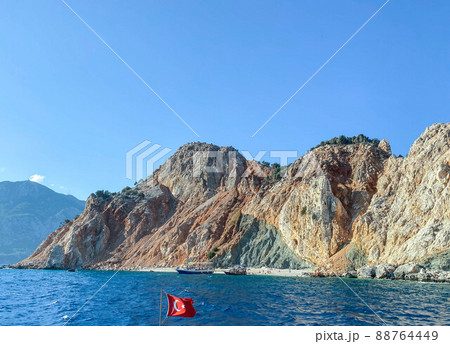 rock in the center of the sea. blue water with bubbling foam with a large, high mountain in the center. sandy rocks. vacation in a warm country. Turkish flag flying nearby rock in the center of the sea. blue water with bubbling foam with a large, high mountain in the center. sandy rocks. vacation in a warm country. Turkish flag flying nearby 88764449