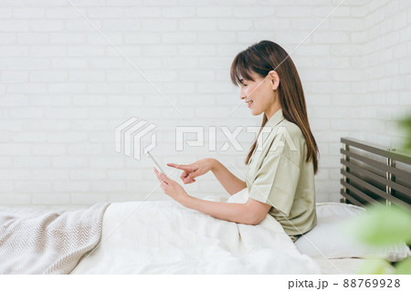 ベッドでスマホを使うミドル世代の女性（笑顔） 88769928