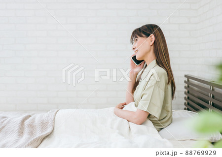 ベッドでスマホを使うミドル世代の女性(通話・笑顔) ベッドでスマホを使うミドル世代の女性(通話・笑顔) 88769929