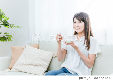 ソファでヨーグルトを食べる女性(笑顔) ソファでヨーグルトを食べる女性(笑顔) 88772121