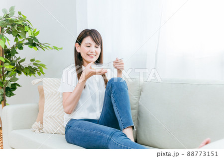 ソファでヨーグルトを食べる女性(笑顔) ソファでヨーグルトを食べる女性(笑顔) 88773151