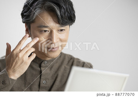 鏡に向かってBBクリームを塗るアラフィフの男性　メンズメイク　イメージ 88777070