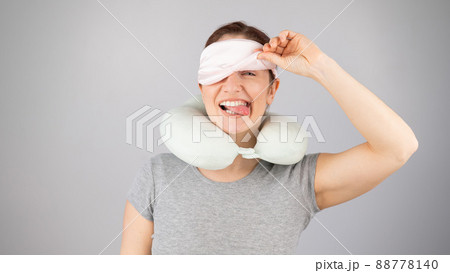 Smiling caucasian woman with a travel pillow takes off her sleep mask on a white background. 88778140