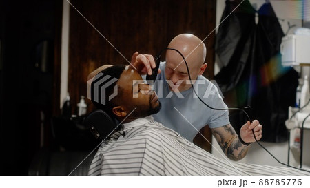 White guy doing a haircut to a young joyful african american guy in a beautiful barbershop White guy doing a haircut to a young joyful african american guy in a beautiful barbershop 88785776