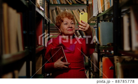 An elderly woman takes a photo with books in the library. Selfie for social networks 88785778