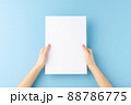 Young woman hands holding blank paper sheet on blue background. Mockup 88786775