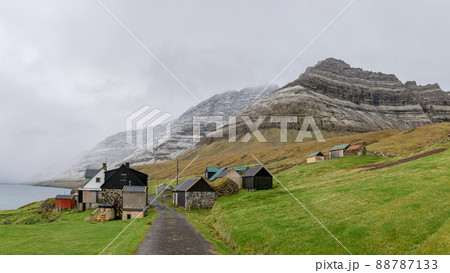 Bour, Faroe Islands - August 2019: A small settlement village overlooking a fjord surrounded by green and snowy mountains Bour, Faroe Islands - August 2019: A small settlement village overlooking a fjord surrounded by green and snowy mountains 88787133