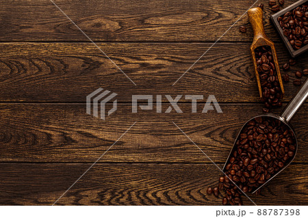Wooden table with coffee beans in scoop composition. Vintage wood background texture and old spoons with grains top view Wooden table with coffee beans in scoop composition. Vintage wood background texture and old spoons with grains top view 88787398