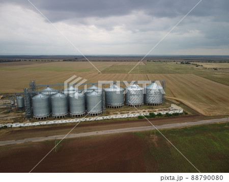 Grain elevator. Metal grain elevator in agricultural zone. Agriculture storage for harvest. Grain elevators on green nature background. Exterior of agricultural factory. Nobody. Grain elevator. Metal grain elevator in agricultural zone. Agriculture storage for harvest. Grain elevators on green nature background. Exterior of agricultural factory. Nobody. 88790080
