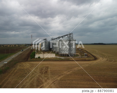 Grain elevator. Metal grain elevator in agricultural zone. Agriculture storage for harvest. Grain elevators on green nature background. Exterior of agricultural factory. Nobody. Grain elevator. Metal grain elevator in agricultural zone. Agriculture storage for harvest. Grain elevators on green nature background. Exterior of agricultural factory. Nobody. 88790081