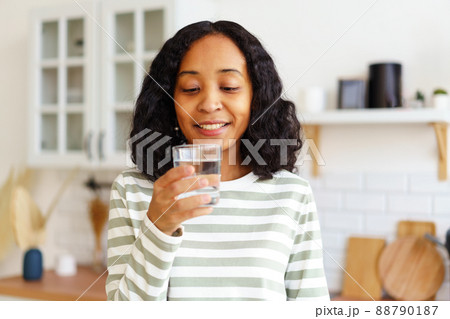 Smiling African-American female enjoying glass of clear water while standing in kitchen Smiling African-American female enjoying glass of clear water while standing in kitchen 88790187