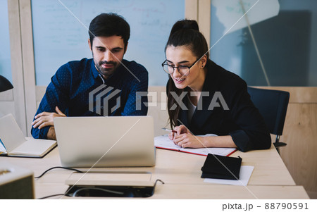 Positive coworkers working with program on laptop and writing down comments in notebooks 88790591