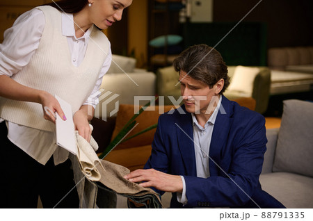 Choosing upholstery fabric color and texture from various colorful samples in a store. Sales assistant and customer hands touching textile. Choosing upholstery fabric color and texture from various colorful samples in a store. Sales assistant and customer hands touching textile. 88791335