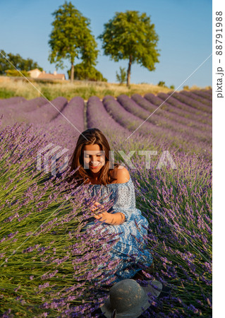 The beautiful young girl in a blue dress sits on the field of a lavender flowers, long curly hair, bright smile, a house of the gardener, trees, perspective of a lavender The beautiful young girl in a blue dress sits on the field of a lavender flowers, long curly hair, bright smile, a house of the gardener, trees, perspective of a lavender 88791988