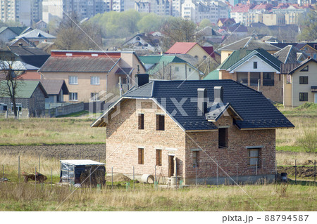 Brand new spacious brick two story residential house with tiling roof and windows openings in suburban neighborhood on background of distant city.Building, mortgage and rel estate property. Brand new spacious brick two story residential house with tiling roof and windows openings in suburban neighborhood on background of distant city.Building, mortgage and rel estate property. 88794587