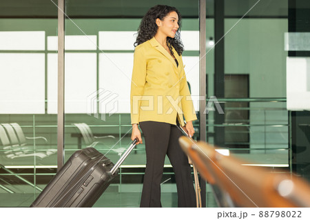 In the airport, a pretty smiling female flight attendant carries luggage to the plane. In the airport, a pretty smiling female flight attendant carries luggage to the plane. 88798022