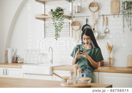 Happy young asian woman relaxing at home she is standing at counter kitchen 88798974