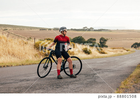 Pro bike female rider wearing helmet and sunglasses training outdoors on empty countryside road 88801508