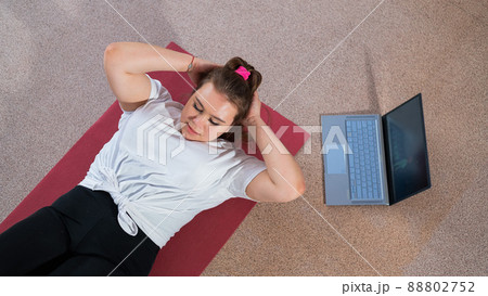 A chubby young woman is watching an online fitness lesson on a laptop. Distance sports training. 88802752