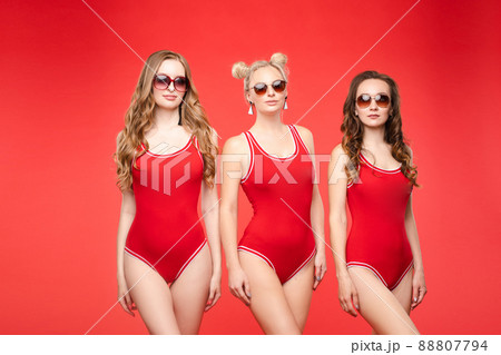 Three women in red swimsuits on a red background Three women in red swimsuits on a red background 88807794