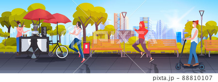 seller in mask standing near small street food market with cupcakes and coffee people relaxing in urban park seller in mask standing near small street food market with cupcakes and coffee people relaxing in urban park 88810107