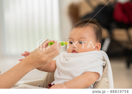 Side view mother feeding her asian baby daughter with pumpkin mashed or vegetable mash on rubber spoon.Mom trying to feed little baby boy at home enjoy and spending time together.Baby feeding Concept 88819758
