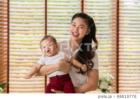 Happy asian mom playing and spending time with her newborn baby and looking at camera together at home.Adorable baby boy smile laughing with mother in warmth place relax and comfortable.good moment 88819776