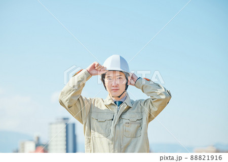 青空を背景にヘルメットをかぶる作業服姿の若い男性 88821916